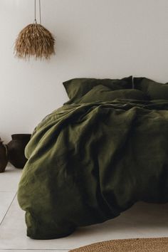 a bed with green sheets and pillows in a room next to a wall hanging from the ceiling