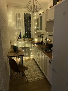 a small kitchen with white cabinets and lights on the windows above the sink, along with a dining room table