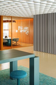 an empty room with a table and stools in front of a wall that has metal slats on it