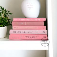 a stack of pink books sitting on top of a white shelf next to a potted plant