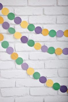 a white brick wall with some paper circles on it and a string of green, yellow, purple, and pink