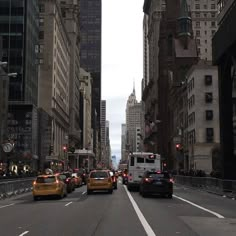 several cars driving down a city street with tall buildings in the background