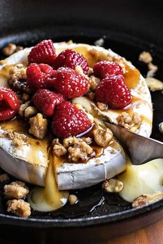 a pancake with raspberries and walnuts on top is being drizzled with syrup