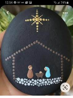 a hand holding a rock with a nativity scene painted on it's side