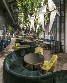 the interior of a restaurant with green velvet seating and plants hanging from the ceiling above