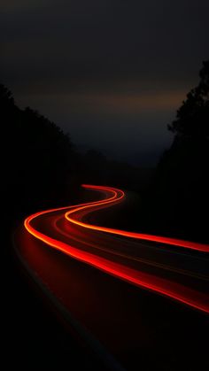 car lights streaking through the night sky on a dark road with trees in the background