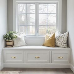 a white window seat with pillows and plants on the windowsill in front of it