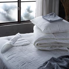 an unmade bed with pillows and blankets on it in front of a large window