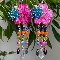 two pink flowers are hanging from earrings with colorful beads and crystal drops on the ends