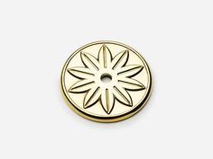 a gold colored metal button with a flower design on the front and center, set against a white background