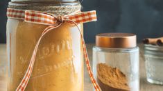 a jar filled with brown liquid next to a cinnamon stick and some spices on a table