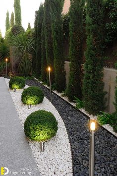 an outdoor garden with gravel, rocks and plants in the center is lit by two lights