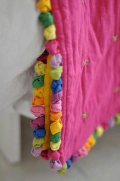 a close up of a bed with a pink blanket and colorful beads on the edge