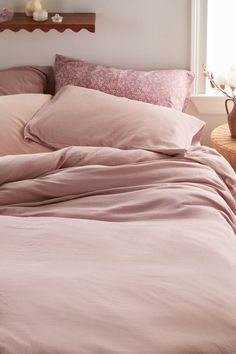 a bed with pink sheets and pillows in a bedroom next to a lamp on a table