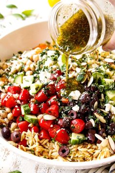 someone pouring olives, tomatoes, and other ingredients into a salad in a bowl