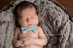 a baby wearing a blue bow tie laying in a wicker basket with his eyes closed