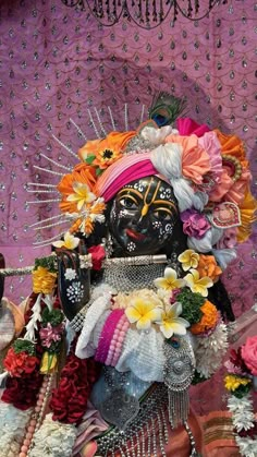 an idol is displayed in front of a purple wall with flowers and beads on it