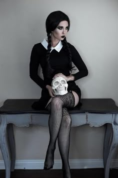 a woman sitting on top of a table with a skull in her hand and wearing fishnet stockings