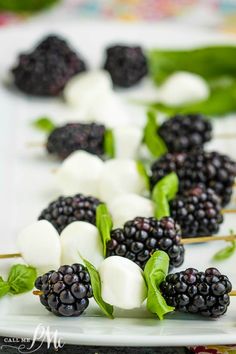 blackberries and mozzarella skewers on a white plate with green leaves