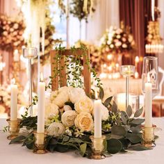 a table with candles, flowers and greenery on it in front of a chandelier