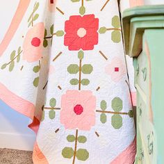 a white and pink quilt sitting on top of a bed next to a green dresser