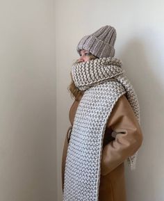 a woman wearing a knitted scarf and beanie standing in front of a wall