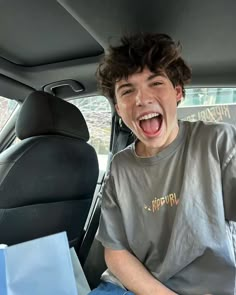 a boy sitting in the back seat of a car with his mouth open