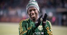 a soccer player wearing a green and yellow uniform holding his hands up in the air