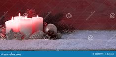 three lit candles surrounded by christmas decorations and pine cones on a snow covered ground with red background