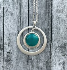 a silver and turquoise necklace on a wooden surface with a circular pendant hanging from it's center