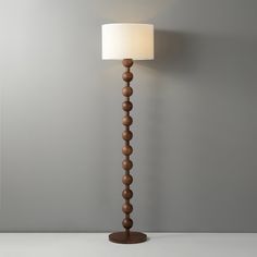 a floor lamp with a white shade on it's side and a gray wall in the background