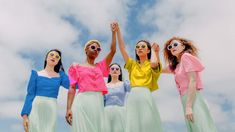 four women are standing together and holding their hands up in the air with one woman wearing sunglasses