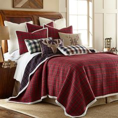 a bed with red and black plaid comforter in a room next to a window