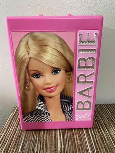 a barbie doll with blonde hair and blue eyes in a pink plastic box that says barbie