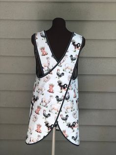 a white vest with farm animals on it and black trim around the neck, hanging from a mannequin