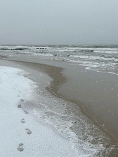 footprints in the snow on a beach next to the ocean