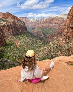 a woman sitting on the edge of a cliff looking out at canyons and mountains