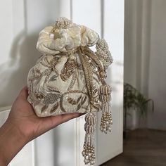 Add a touch of elegance and sophistication to your bridal look with our exquisite Cream Velvet Potli Bag. Crafted from premium velvet, this potli bag is a testament to timeless beauty and unmatched craftsmanship. The soft cream shade exudes a subtle charm that complements any bridal attire, while the intricate hand-embroidered zardozi and sequins work create a mesmerizing display of artistry. Each stitch and sequin is meticulously placed, showcasing the skill and dedication of our artisans. Designed for comfort and style, this potli bag features a stunning handmade braided handle adorned with delicate beads, offering both durability and a unique aesthetic. The handle is carefully crafted to ensure a comfortable grip, making it an ideal accessory for the bride on her special day. To further Eastern Wear, Potli Bag, Bridal Attire, Desi Bride, Wristlet Bag, Bridal Bag, Potli Bags, Wedding Bag, Pakistani Wedding