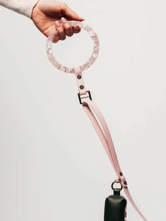 a hand holding a pink leash with a bell attached to it and a round ring on the end