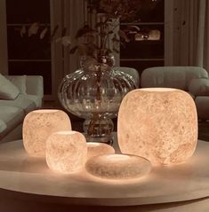 a table with some lights on it in front of a couch and coffee table next to a vase