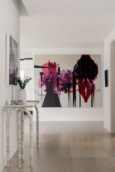 an abstract painting hangs on the wall next to a console