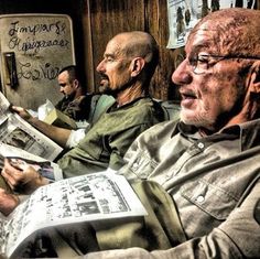 two men sitting on a train reading newspapers while another man looks at the newspaper in his hand