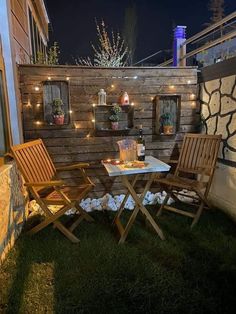 two wooden chairs sitting on top of a grass covered field next to a small table