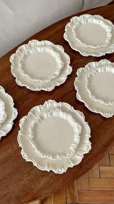 four white plates sitting on top of a wooden table next to a pillow and chair