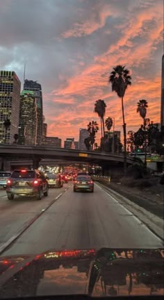 cars driving down the highway at dusk with palm trees and buildings in the back ground