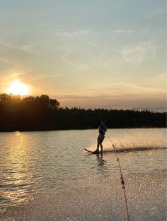 a person riding skis on top of a body of water near the shore at sunset