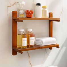 two wooden shelves with bottles and soaps on them in a white bathroom, against a marble wall