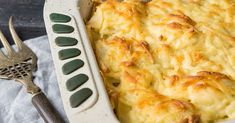 a casserole dish with cheese and bread in it next to a silver utensil