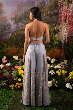 Element of fun and ethereal crafted in one ensemble. Sofia co-ord set consists of a halter neck top paired up with wide-legged pants accentuated with tassel drops. The ice-blue hue of the ensemble makes one look surreal and elegant while at the same time, the silhouette defines your bubbliness. Halter neck blouse embroidered with daisy motifs highlighted with sequins and flowers. Wide-legged pants with attached crisscross studded straps at the waistline crafted out of blingy sequined fabric high