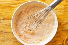 a white bowl filled with batter and whisk on top of a wooden table